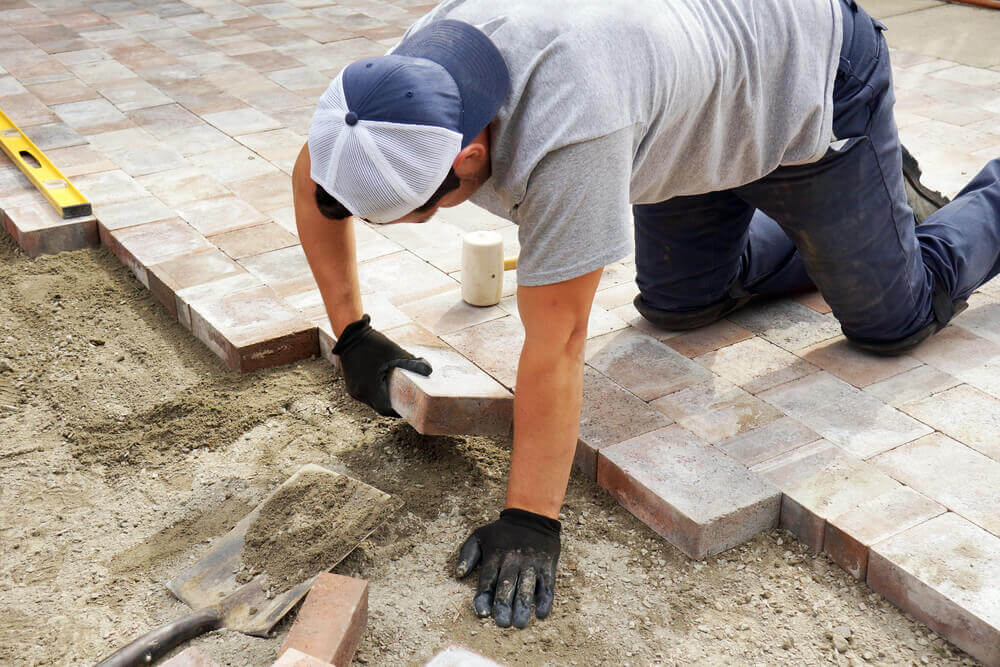 a paving Ballarat worker laying down some pavers with black gloves on and a level close by