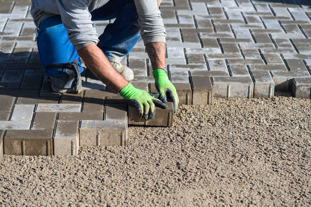 a paving Ballarat worker with green safety gloves on laying a single brick amongst many other bricks that have been laid